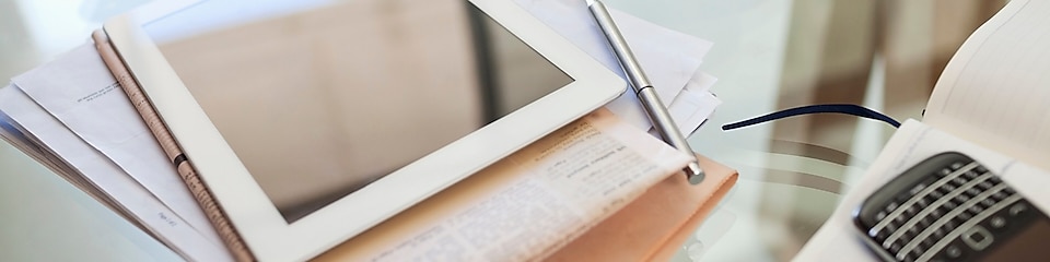 Tablet computer, newspaper, coffee cup and cell phone on desk