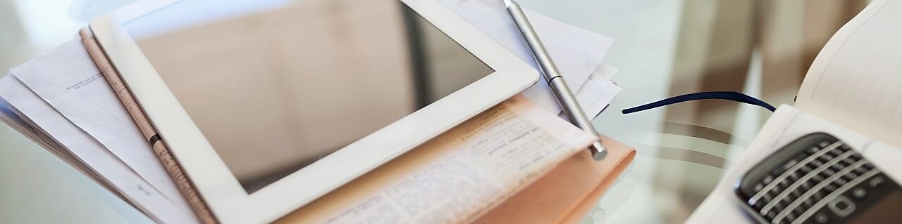 Tablet computer, newspaper, coffee cup and cell phone on desk